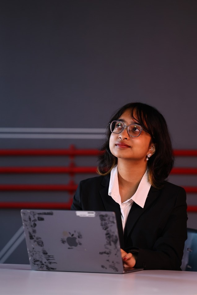 A student looking up thoughtfully, laptop open in front of her
