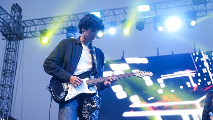 A student performing on guitar under stage lights at the fest